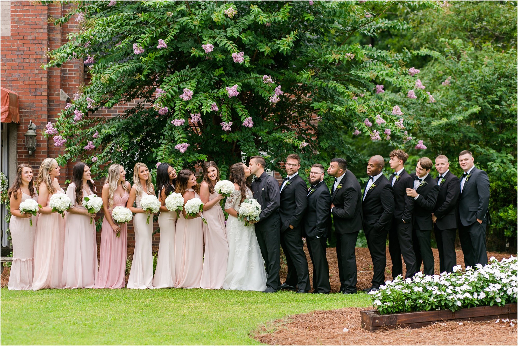 blush, pink, and white bridal party by pink tree and lush grass