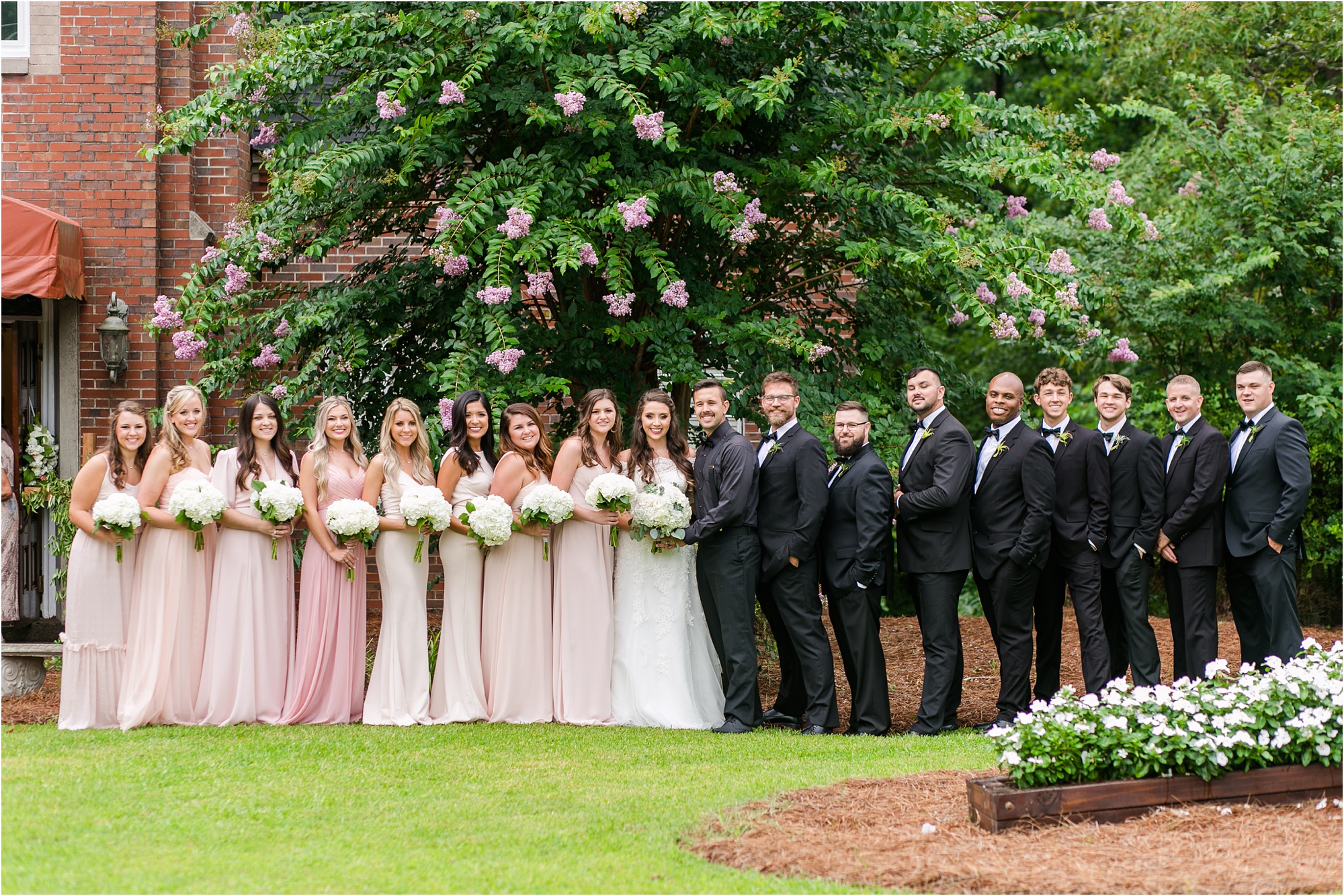 blush, pink, and white bridal party by pink tree and lush grass